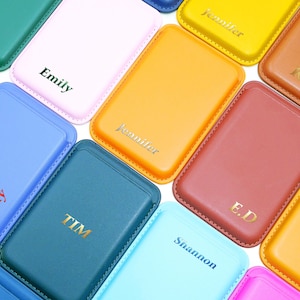 Pode incluir: Uma coleção de porta-cartões de couro personalizados em várias cores, incluindo rosa, azul e castanho. Cada porta-cartões é gravado com um nome ou iniciais em tom dourado. Os porta-cartões têm formato retangular com cantos arredondados e bordas costuradas.