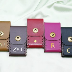 Puede incluir: Cinco estuches de cuero en varios colores: marrón, marrón oscuro, rojo, magenta y negro. Cada estuche tiene un cierre de botón a presión y bordes cosidos. Los estuches están personalizados con letras doradas o plateadas.