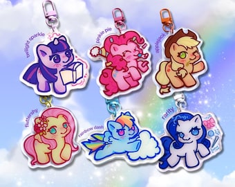 May include: Six colourful My Little Pony character keychains. Each keychain features a different pony design with names like Twilight Sparkle, Pinkie Pie, and Rainbow Dash. They have silver-coloured clasps and are set against a pastel background.