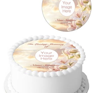 Pode incluir: Um bolo branco com um topper comestível redondo. O topper apresenta um fundo de pôr do sol, lírios brancos e o texto "In Loving Memory of", "Your Image Here", "Name Surname" e "Date Date". O bolo tem 19 cm de diâmetro.
