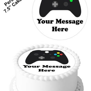 Peut inclure: Un topper de gâteau rond de 7,5 pouces avec une illustration en noir et blanc d'une manette de jeu vidéo. Le texte "Your Message Here" est imprimé sous la manette.