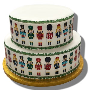 Könnte beinhalten: Eine zweistöckige weiße Torte, verziert mit einem grünen Kranz und einem sich wiederholenden Muster aus bunten Nussknackerfiguren.