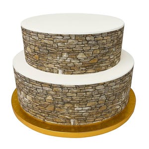 May include: A two-tiered cake with a stone wall design. The cake has a white top and a gold base. The sides of the cake are decorated with a detailed pattern of various-sized stones in shades of brown, gray, and beige.