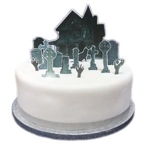 May include: A white cake decorated with a haunted house and tombstones. The cake is on a silver cake board.