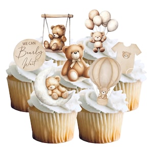 May include: Decorated cupcakes with teddy bear toppers, including a bear on a swing, holding balloons, and in a hot air balloon. The cupcakes are baby-themed, with the phrase "We Can Bearly Wait" on a circular sign.