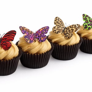 Pode incluir: Quatro cupcakes com cobertura bege e formas de papel castanho-escuro. Cada um é decorado com uma borboleta decorativa em várias cores e padrões, incluindo vermelho, roxo e estampa de leopardo. Os cupcakes estão dispostos em uma fileira contra um fundo branco.