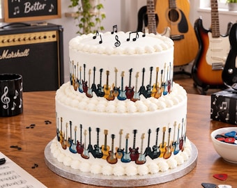 May include: A two-tier white frosted cake decorated with a repeating pattern of various electric and acoustic guitars around the sides. The top of the cake features black musical note toppers. The cake sits on a silver circular base.