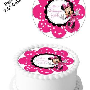 Op de afbeelding: Een ronde, eetbare taarttopper van 19 cm doorsnee met Minnie Mouse in een roze jurk met witte stippen. De topper is op een witte taart met witte frosting. De topper heeft de vorm van een roze bloem met witte stippen en een zwarte cirkel met de tekst "Your Message Here".