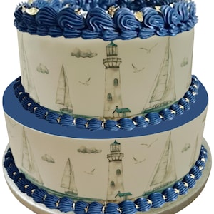 May include: A two-tiered cake decorated with blue frosting and a nautical themed edible image. The image features a lighthouse, sailboats, and seagulls against a light blue sky.