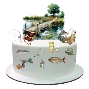 Peut inclure: Un gâteau blanc décoré d'une scène de pêche. La scène comprend une jetée en bois, un lac, des nénuphars, des poissons, des cannes à pêche, une chaise de pêche, une boîte à pêche et un chapeau de pêche.