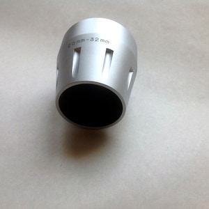 Op de afbeelding: Een zilverkleurig metalen object met een zwarte binnenkant. Het cilindrische object heeft verticale uitsparingen en de tekst "20mm-32 mm". Het is waarschijnlijk een gereedschap of onderdeel.