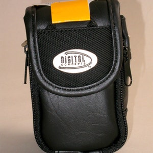 May include: Black camera case with a mesh front panel and a zipper closure. The case has a leather-like texture and features the "DIGITAL CONCEPTS" logo on the front. A bright yellow tag is attached to the top.