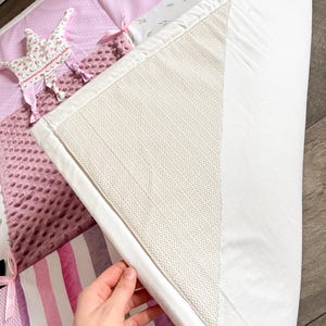 May include: A patchwork baby play mat with various pink and white patterns, including stripes, polka dots, and floral designs. The mat features a soft, textured surface and a white border. Decorative star-shaped accents and ribbons are visible.