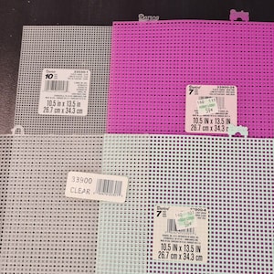 May include: Assortment of plastic canvas sheets in various colors, including gray, pink, and light green. Each sheet is 10.5 inches by 13.5 inches. Labels with product information are visible.
