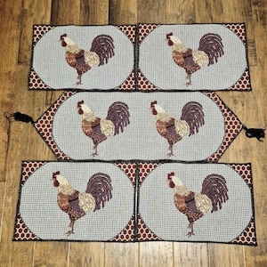 May include: Set of six rooster-themed placemats. Each placemat features a detailed rooster illustration in shades of brown, beige, and purple against a light blue background. The edges are bordered with a dark red and brown polka dot pattern.