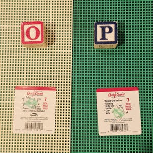 May include: Two sheets of 7-mesh plastic canvas, one beige and one green, each featuring a Quick Count label. A wooden block with a red letter O sits on the beige sheet, and a wooden block with a blue letter P sits on the green sheet.