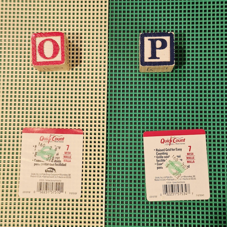 May include: Two sheets of 7-mesh plastic canvas, one beige and one green, each featuring a Quick Count label. A wooden block with a red letter O sits on the beige sheet, and a wooden block with a blue letter P sits on the green sheet.