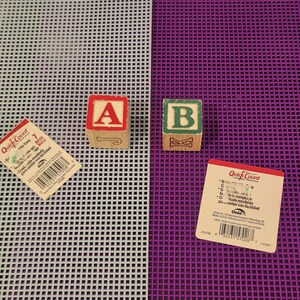 May include: Two wooden alphabet blocks, one with a red A and J, the other with a green B and K, placed on light gray and purple plastic mesh sheets. Two QuickCount product labels with barcodes and text are positioned near the mesh sheets.