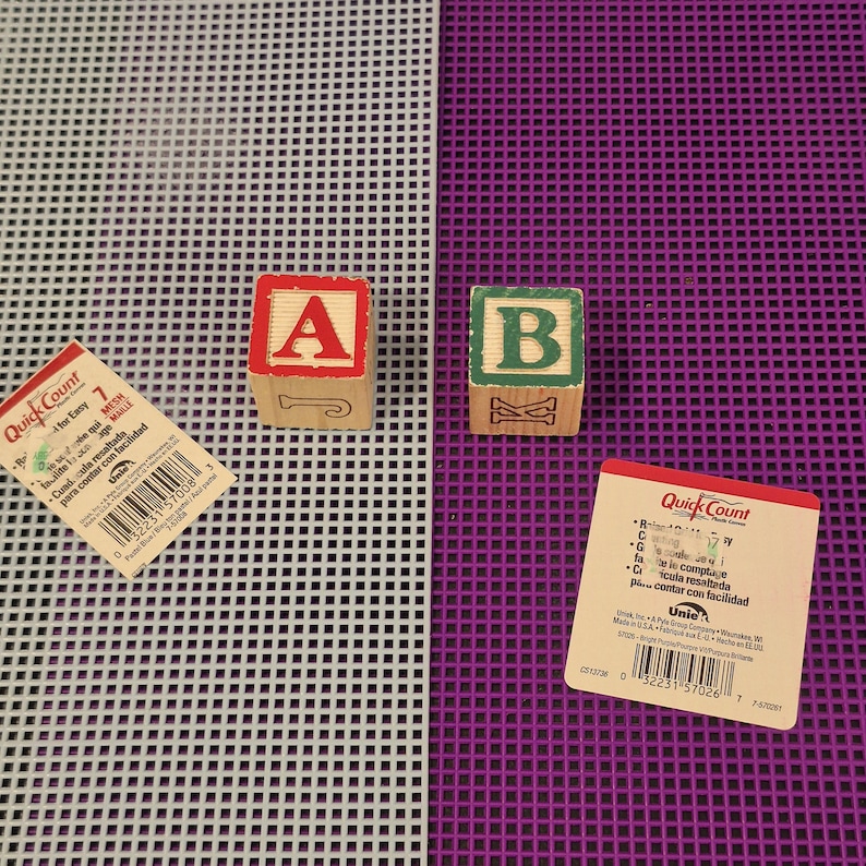 May include: Two wooden alphabet blocks, one with a red A and J, the other with a green B and K, placed on light gray and purple plastic mesh sheets. Two QuickCount product labels with barcodes and text are positioned near the mesh sheets.
