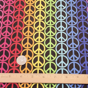 May include: A black fabric with a repeating pattern of colorful peace symbols in a rainbow gradient. The peace signs are in shades of pink, red, orange, yellow, green, blue, and purple. A ruler is at the bottom of the image.