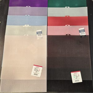 May include: A collection of ten rectangular plastic canvas sheets in various colors including purple, green, light purple, white, light blue, red, pink, beige, and black. Each sheet features a uniform grid pattern and a small tab at the top edge.
