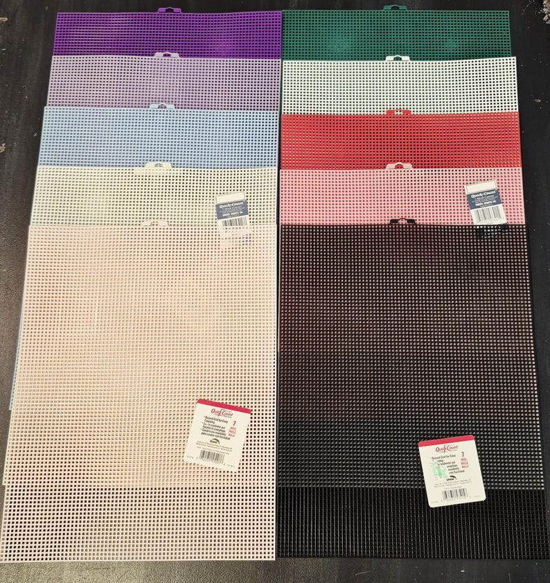 May include: A collection of ten rectangular plastic canvas sheets in various colors including purple, green, light purple, white, light blue, red, pink, beige, and black. Each sheet features a uniform grid pattern and a small tab at the top edge.