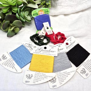 May include: A collection of colorful embroidery floss and thread spools. The spools are in various colors, including blue, yellow, gray, red, and black. The labels indicate the thread is 10 yards (9.1 meters) long and made of silk.