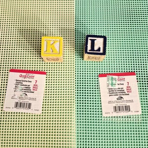 May include: Two square wooden alphabet blocks, one yellow with the letter K and one dark blue with the letter L, placed on two plastic mesh sheets, one ivory and one mint green, each featuring a Quick Count label with a barcode and text.