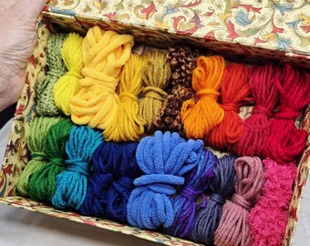 May include: A box filled with colorful yarn bundles in a rainbow of hues. The yarn colors include yellow, orange, red, green, blue, and purple. The box has a decorative floral pattern.