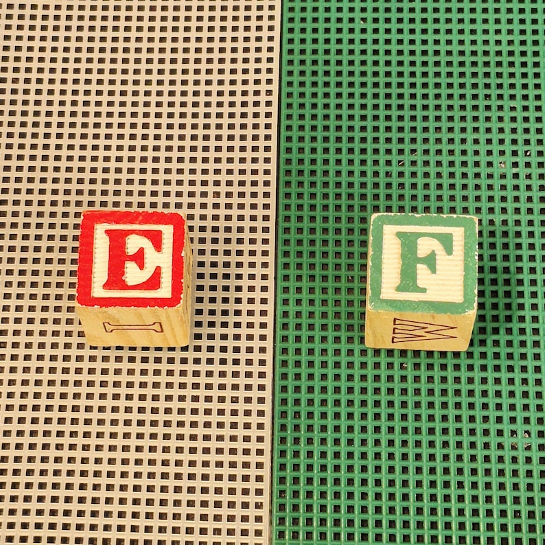 May include: Two wooden alphabet blocks. One block features a red letter E on a white background with a black letter I on the side. The other block features a green letter F on a white background with a black letter W on the side. Both are square.