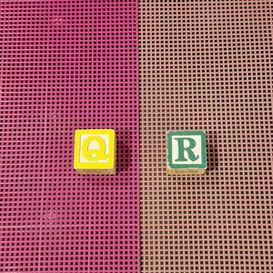 May include: Two square wooden alphabet blocks. The left block is yellow with a bright yellow letter Q. The right block is light green with a dark green letter R. Both blocks feature a distressed, worn finish on their edges and surfaces.