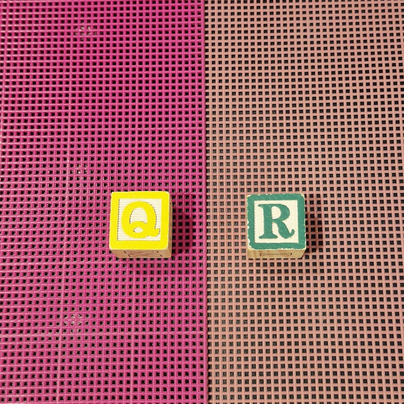 May include: Two square wooden alphabet blocks. The left block is yellow with a bright yellow letter Q. The right block is light green with a dark green letter R. Both blocks feature a distressed, worn finish on their edges and surfaces.