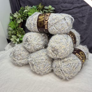 May include: A stack of gray and white Himalaya knitting yarn balls. Each ball has a brown label with gold text. The yarn is soft and fluffy, perfect for knitting or crocheting projects. The background includes a green wreath.