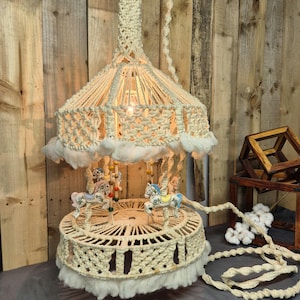 May include: A handmade carousel lamp with a cream-colored macrame design. The lamp features a circular base with miniature carousel horses and a decorative top. The lamp is suspended from a woven cord and has a soft, fluffy trim.