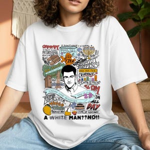 Può includere: T-shirt bianco con una grafica raffigurante un uomo con varie frasi e illustrazioni. Il testo include "Schmidt Happens!" e "A White Man?? No!!". Il design incorpora elementi di cartoni animati e testo scritto a mano.