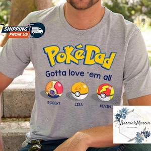 May include: A gray t-shirt with the text "Poke Dad" in yellow and blue, with the phrase "Gotta love 'em all" below. Three colorful Poke Balls are displayed, each with a name: Robert, Lisa, and Kevin. The shirt is a casual wear item.