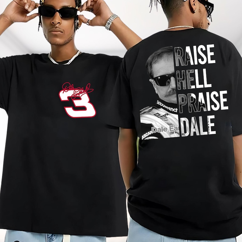 May include: Black t-shirts featuring racing-themed graphics. One shirt displays a red and white number 3 with a signature. The other shirt has a portrait of a man with sunglasses and the words "RAISE HELL PRAISE DALE".