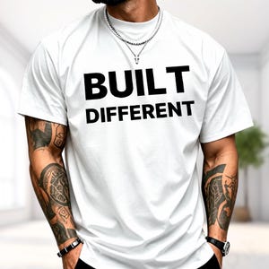 May include: A white short-sleeved t-shirt featuring the text BUILT DIFFERENT printed in bold black capital letters across the chest. The shirt has a crew neckline and a standard fit, providing a clean and simple look for casual wear.