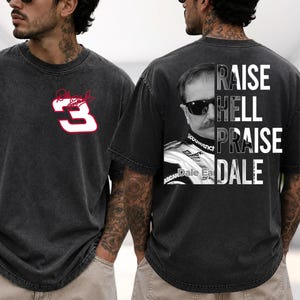 May include: Dark gray t-shirt featuring the number 3 in white with a red outline on the front. The back of the shirt displays a black and white image of a man wearing sunglasses, with the words "RAISE HELL PRAISE DALE".