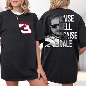 May include: Black t-shirt featuring a white and red number 3 with a signature on the front. The back of the shirt displays a black and white image of a man with sunglasses and the words "RAISE HELL PRAISE DALE".