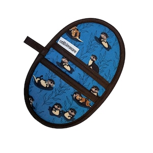 May include: An oval-shaped pot holder with a blue background featuring a pattern of otters and seaweed. The pot holder has brown trim and a brown loop for hanging. The text "collisionware" is visible on the front.