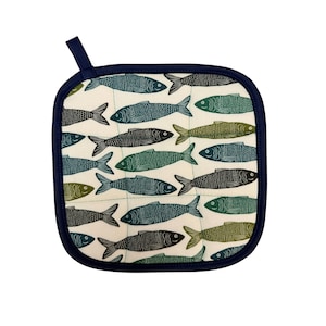 May include: Square off-white pot holder with a navy blue border and hanging loop. The pot holder features a repeating pattern of stylized fish in shades of green, teal, and black. The fish are arranged on a grid.