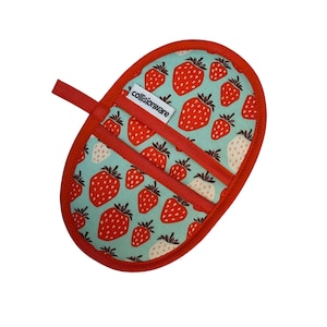 May include: An oval-shaped pot holder with a red border and a loop for hanging. The main fabric is light blue with a pattern of red and white strawberries. The text "collisionware" is visible on a white label.