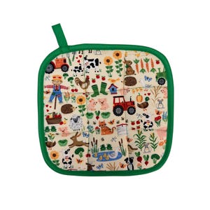 May include: Square quilted pot holder with a green border and hanging loop. The cream-colored fabric is patterned with a farm scene, including a red tractor, scarecrow, animals, and vegetables. The pot holder is approximately 8 inches square.