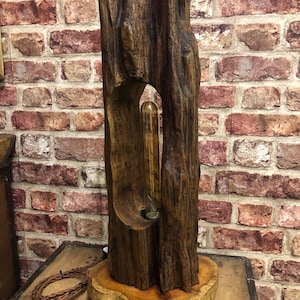 May include: A rustic wooden lamp with a natural, textured finish. The lamp features a hollowed-out section revealing a vintage-style lightbulb. The base is a cross-section of a tree trunk. The lamp is approximately 61 cm tall.