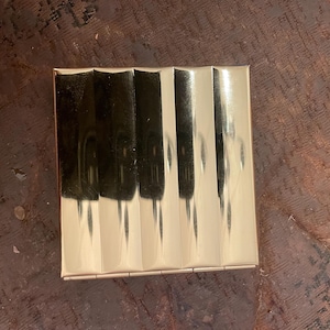 May include: A gold-colored compact with a ribbed design. The compact is closed and has a rectangular shape.