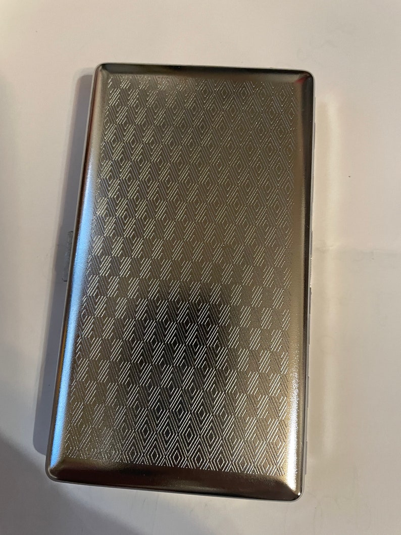 May include: A silver cigarette case with a geometric pattern.