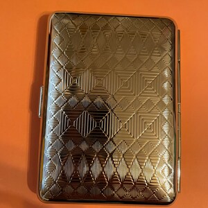 May include: A silver cigarette case with a geometric pattern embossed on the front.