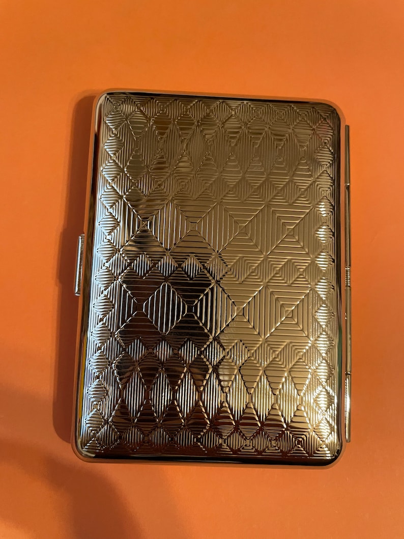 May include: A silver cigarette case with a geometric pattern embossed on the front.