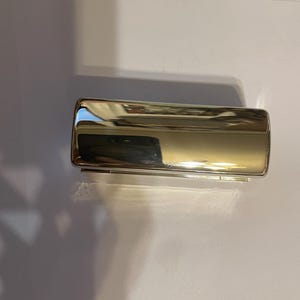 May include: A silver metal cigarette case with a hinged lid.